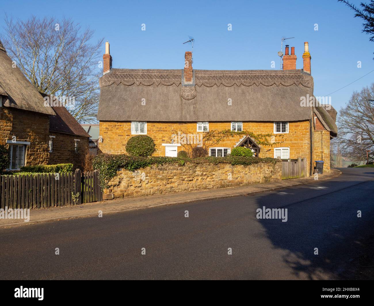 Scena stradale sotto il sole d'inverno, caratterizzata da cottage con tetto in paglia, nel villaggio di Great Brington, Northamptonshire, Regno Unito Foto Stock