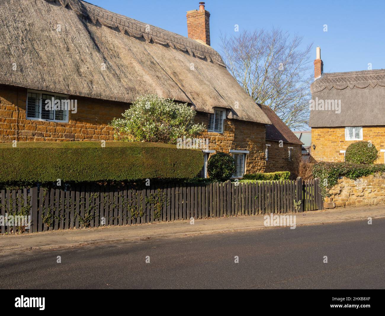 Scena stradale sotto il sole d'inverno, caratterizzata da cottage con tetto in paglia, nel villaggio di Great Brington, Northamptonshire, Regno Unito Foto Stock