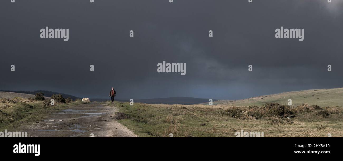 Un'immagine panoramica di spettacolari nuvole di tempesta sopra un uomo che cammina lungo i resti di una pista ferroviaria disutilizzata sul selvaggio e aspro Bodmin Moor in Cornovaglia Foto Stock