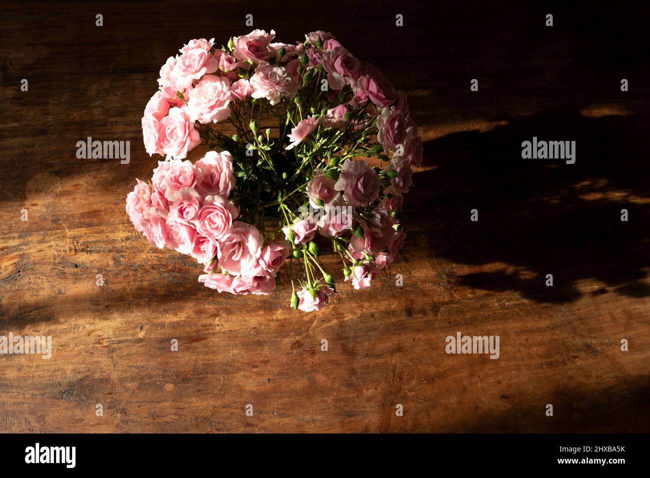mazzo di piccole rose rosa in vaso su tavola di legno alla luce del sole Foto Stock