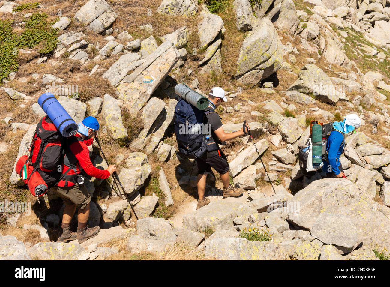 Tre escursionisti maschi in piena estate attrezzature discese tra massi nel Parco Nazionale e Riserva Pirin, Monte Pirin, Bulgaria, Balcani, Europa Foto Stock