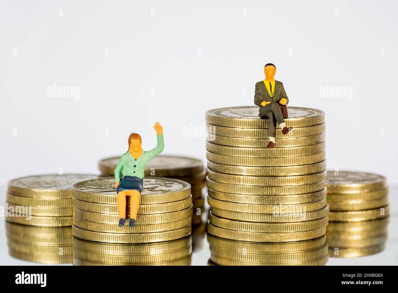 Persone in miniatura sedute su un mucchio di monete. Il concetto di divari nella distribuzione del reddito Foto Stock