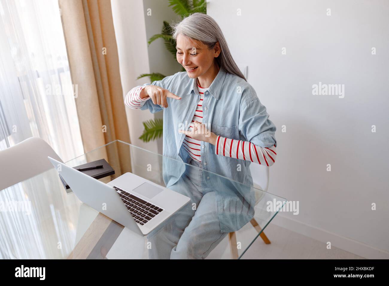 Donna sorridente che usa un notebook per le comunicazioni online a casa Foto Stock