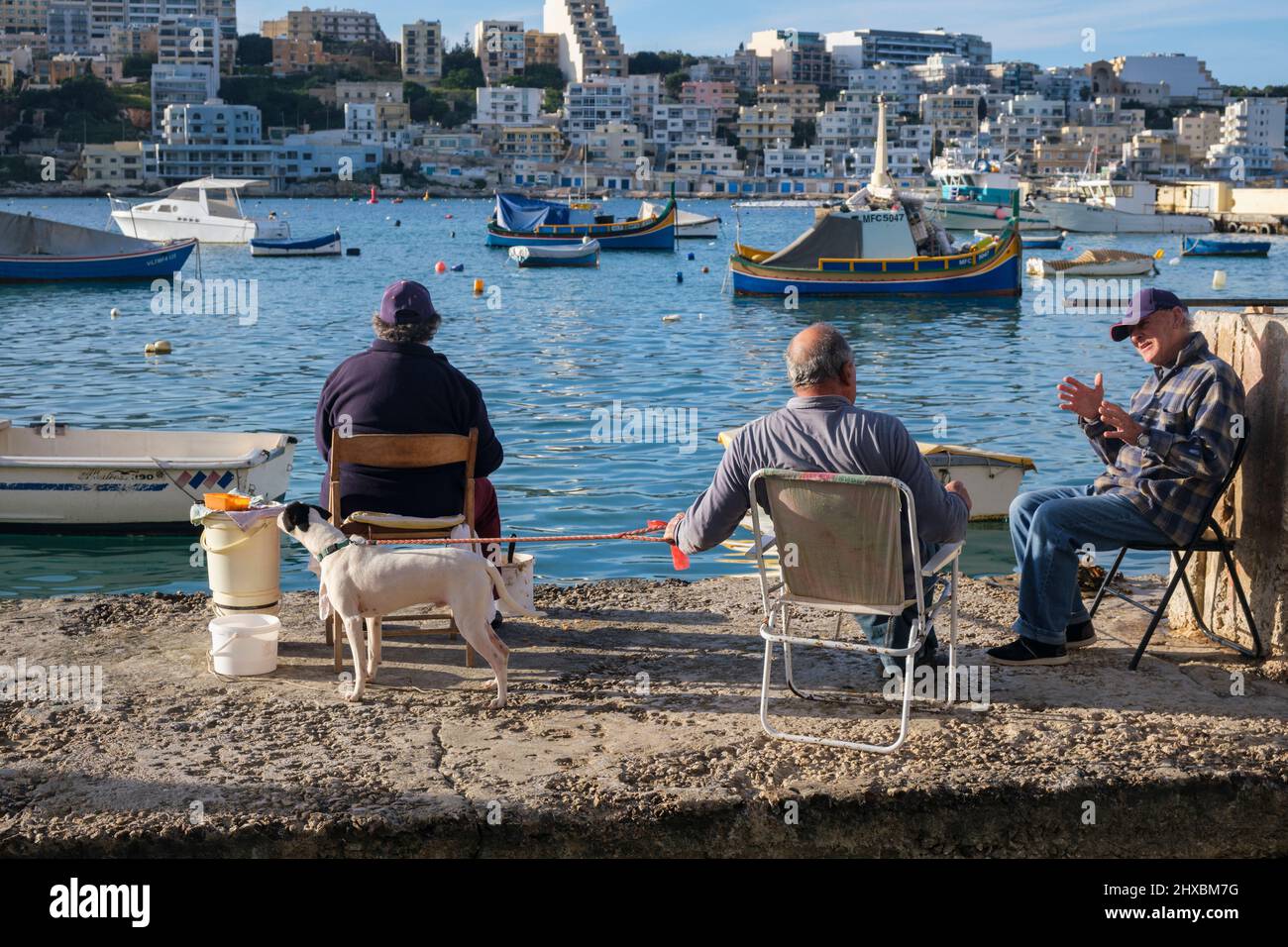 Gli uomini locali pescano e chiacchierano sulla banchina di St Paul's Bay, Malta Foto Stock