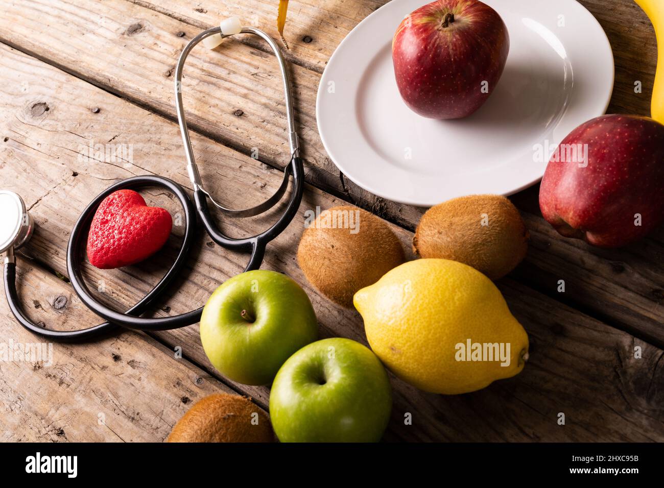 Vista ad angolo alto di vari frutti con stetoscopio e forma a cuore su tavola di legno Foto Stock