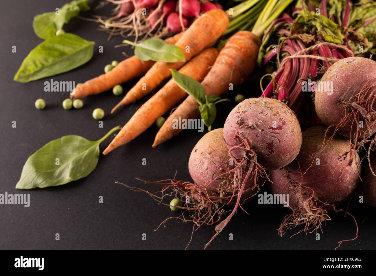 Primo piano di carote e barbabietole con piselli verdi e verdure in foglia su sfondo nero Foto Stock