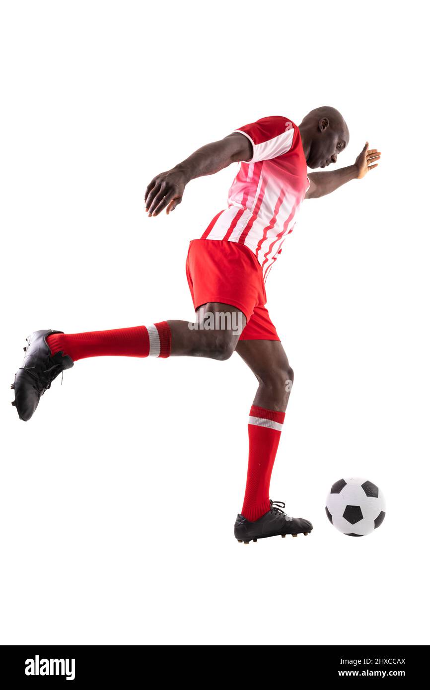 Vista laterale del giovane giocatore di calcio afroamericano maschile che calcia la palla su sfondo bianco Foto Stock