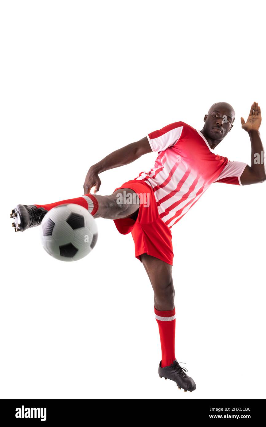 Tutta la lunghezza del giovane atleta maschile africano americano calcia palla di calcio su sfondo bianco Foto Stock