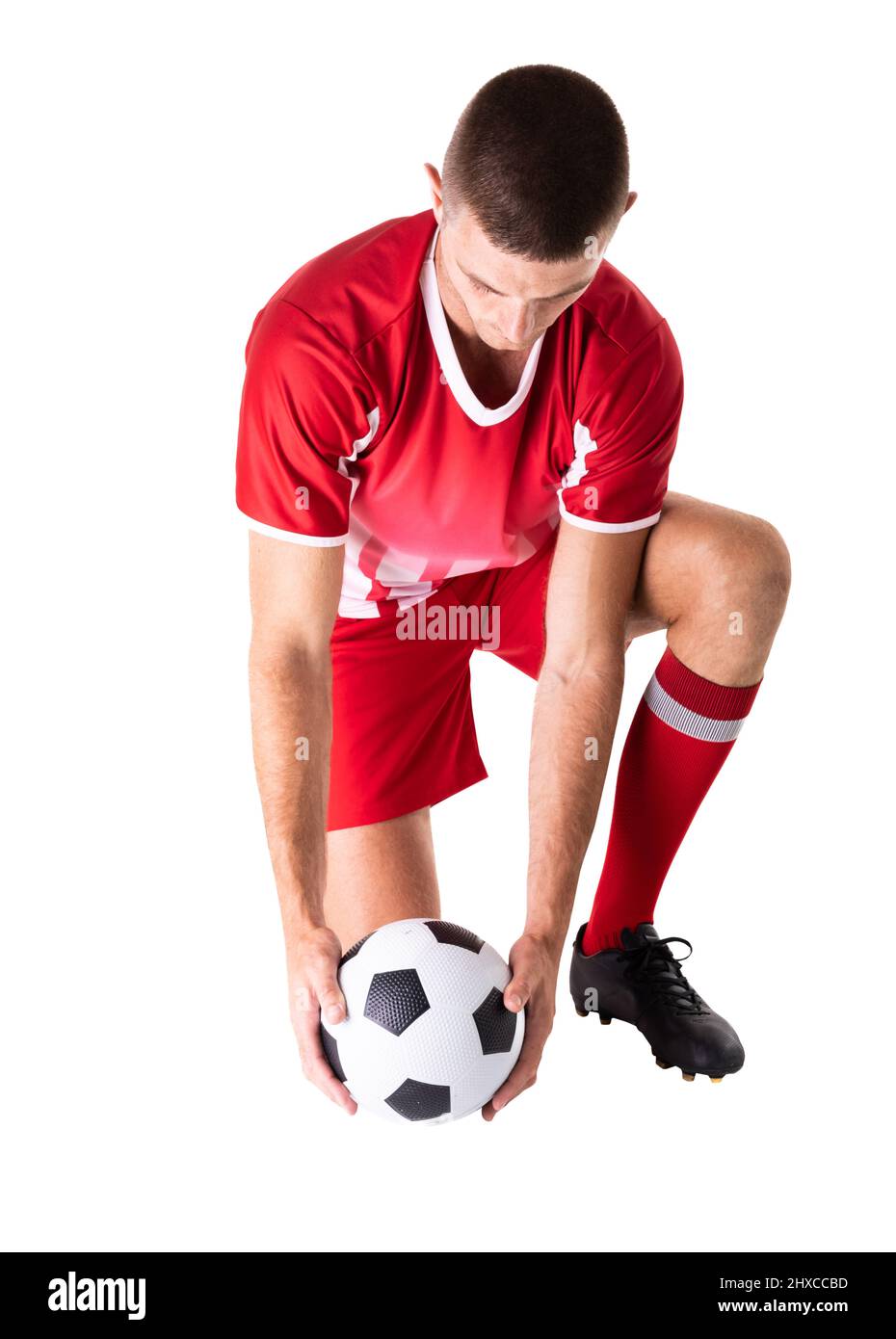 Tutta la lunghezza del giovane calciatore caucasico maschio inginocchiarsi tenendo la palla su sfondo bianco Foto Stock
