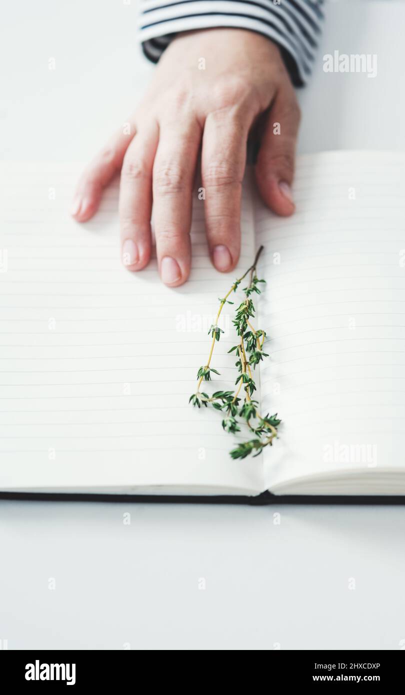 Studiare le piante è che cosa fa. Scatto ritagliato di una mano femminile irriconoscibile che tocca un notebook aperto su cui è posizionato un campione di piante. Foto Stock