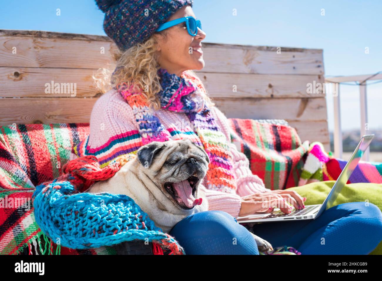 Donna, cappuccio, sciarpa, occhiali da sole, laptop, Lavoro, esterno, panca, coperta, cane, PUG Foto Stock