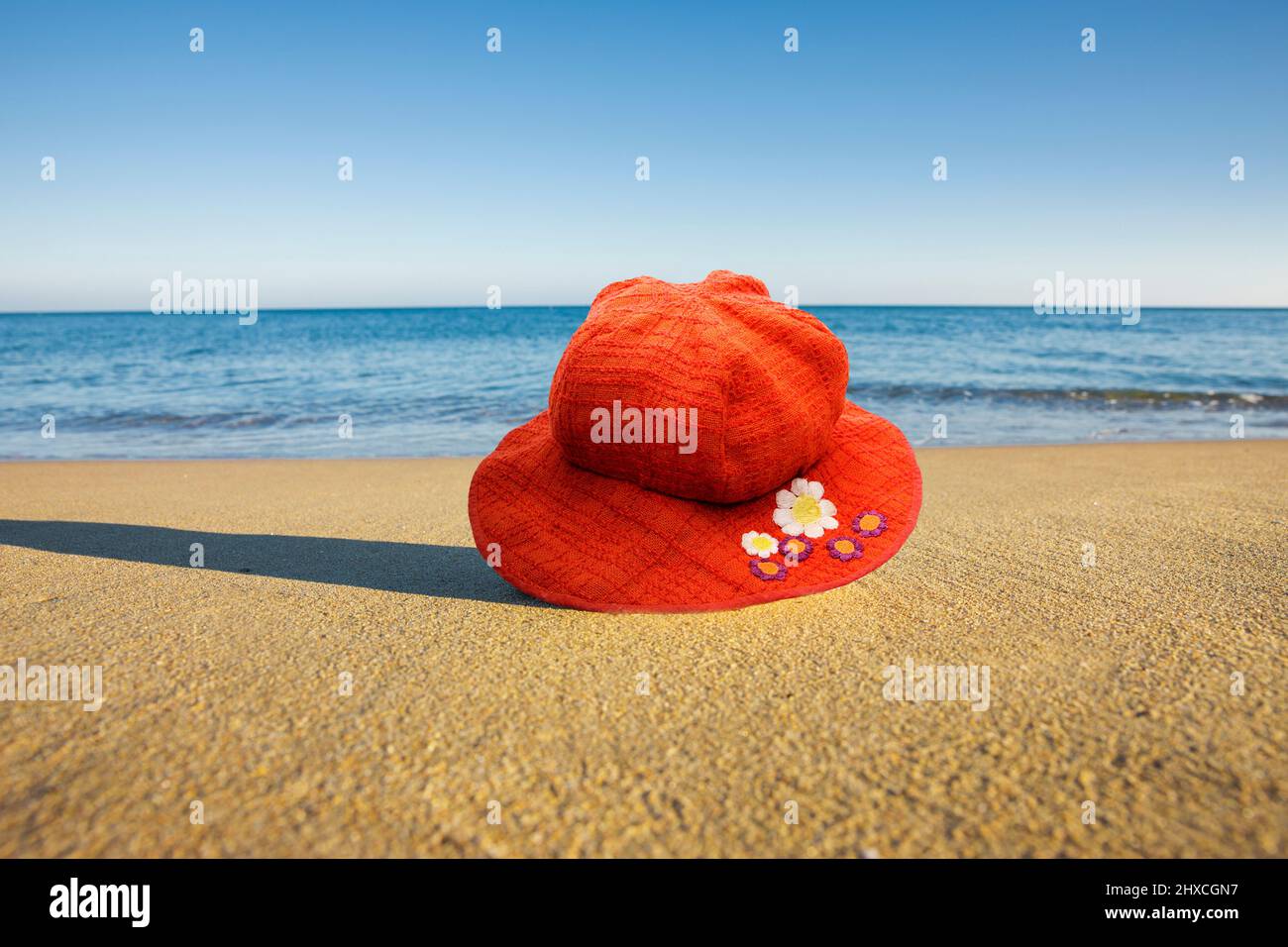 Cappello rosso sulla sabbia accanto al mare blu Foto Stock
