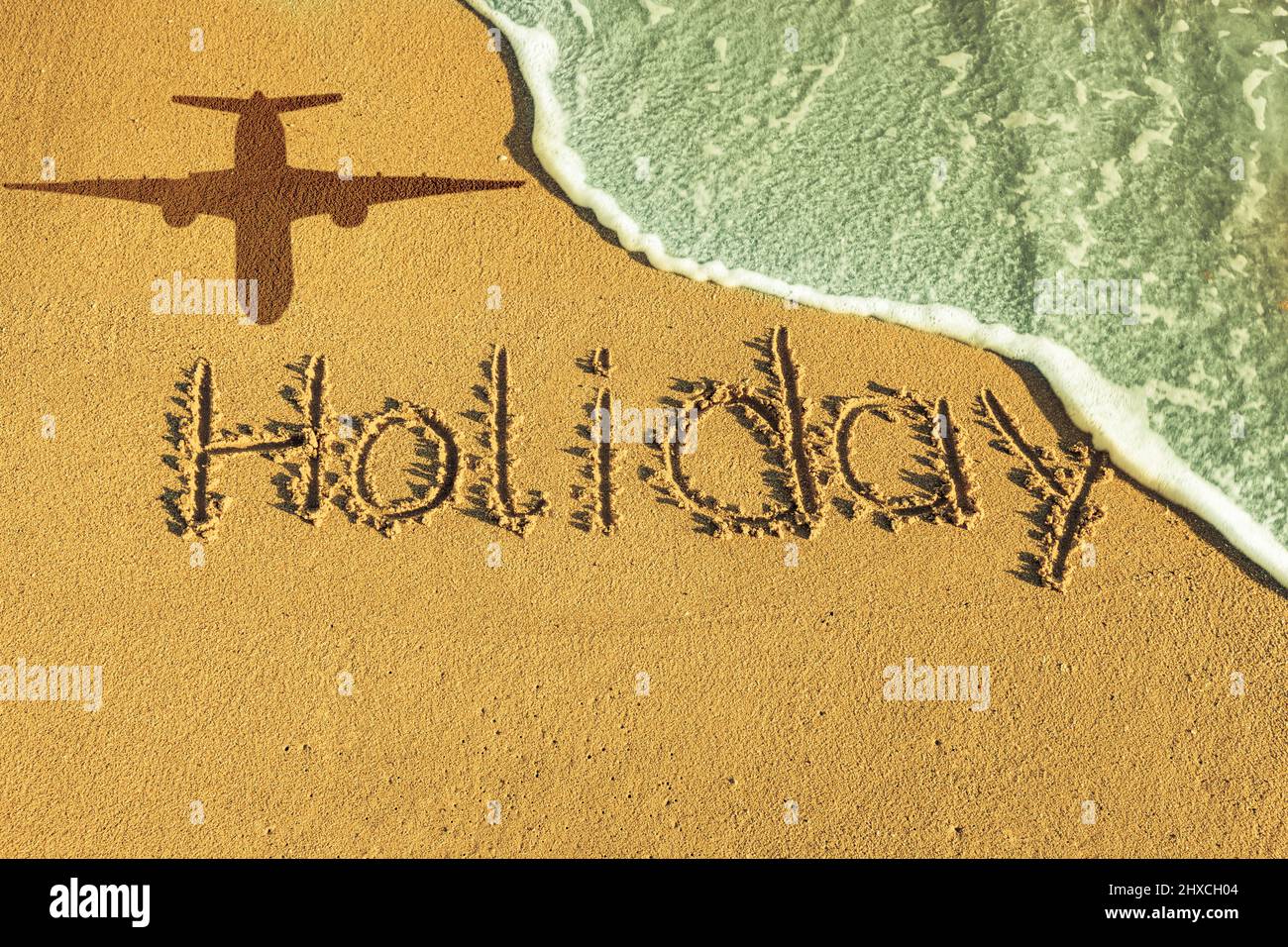 La parola vacanza scritta nella sabbia vicino al mare, ombra di un aereo Foto Stock