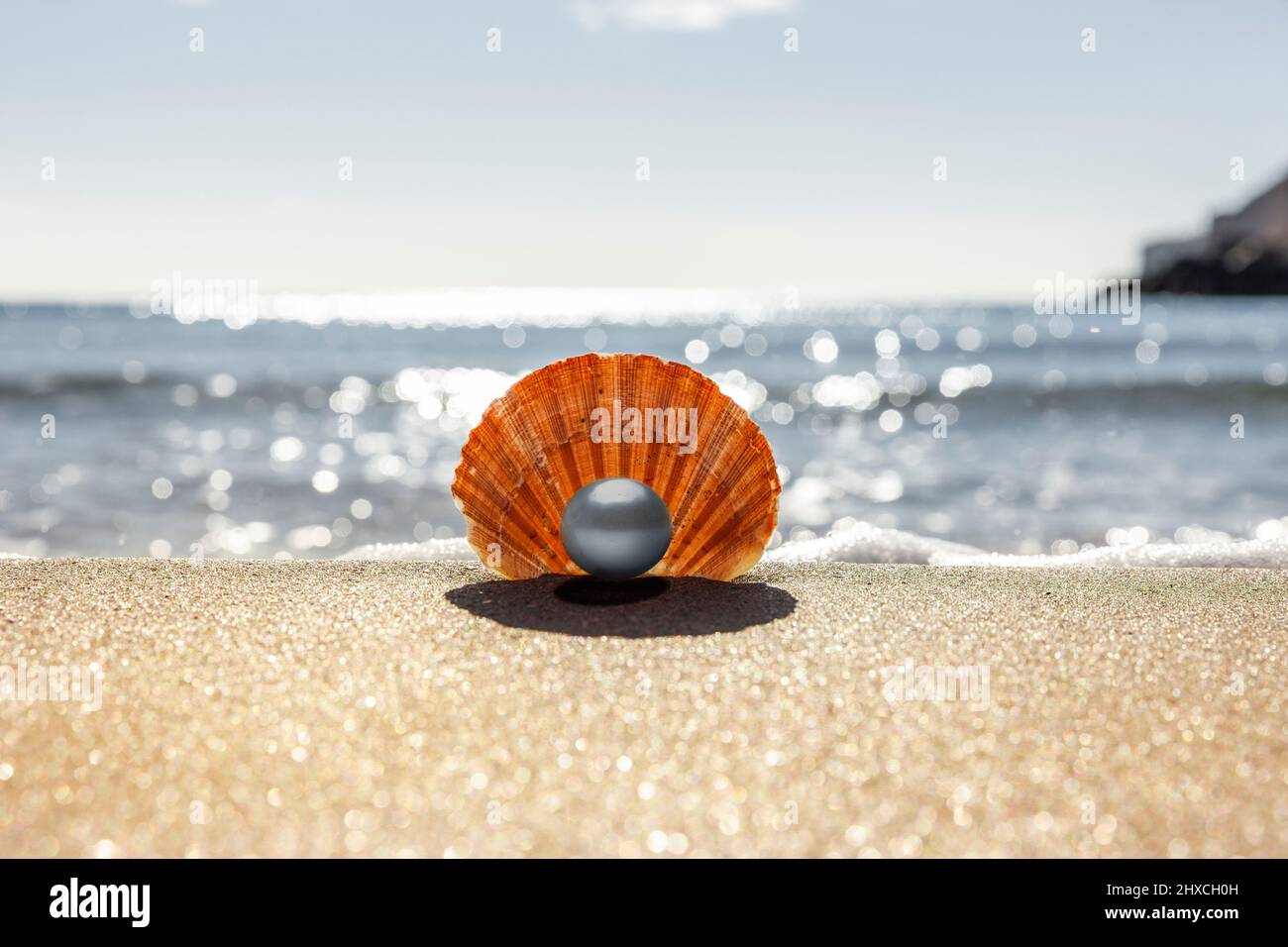 Capesante con perla sulla spiaggia con mare sullo sfondo Foto Stock
