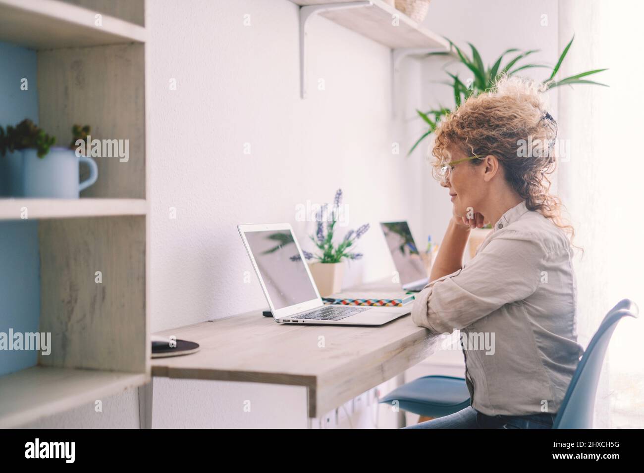 Donna che lavora a casa con un notebook su una workstation desktop. Foto Stock