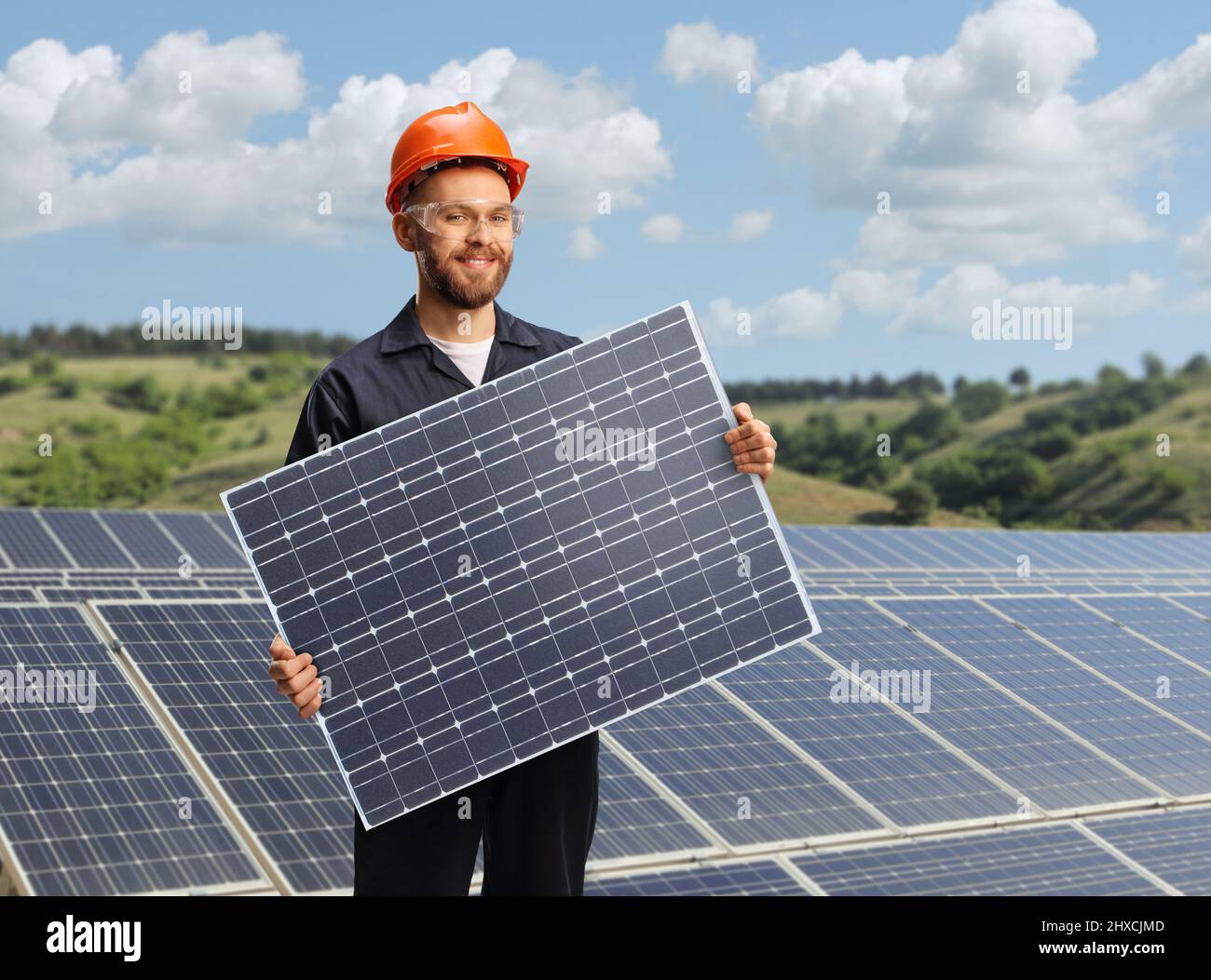 Lavoratore in un unibody che tiene un modulo fotovoltaico a celle solari su una fattoria solare Foto Stock