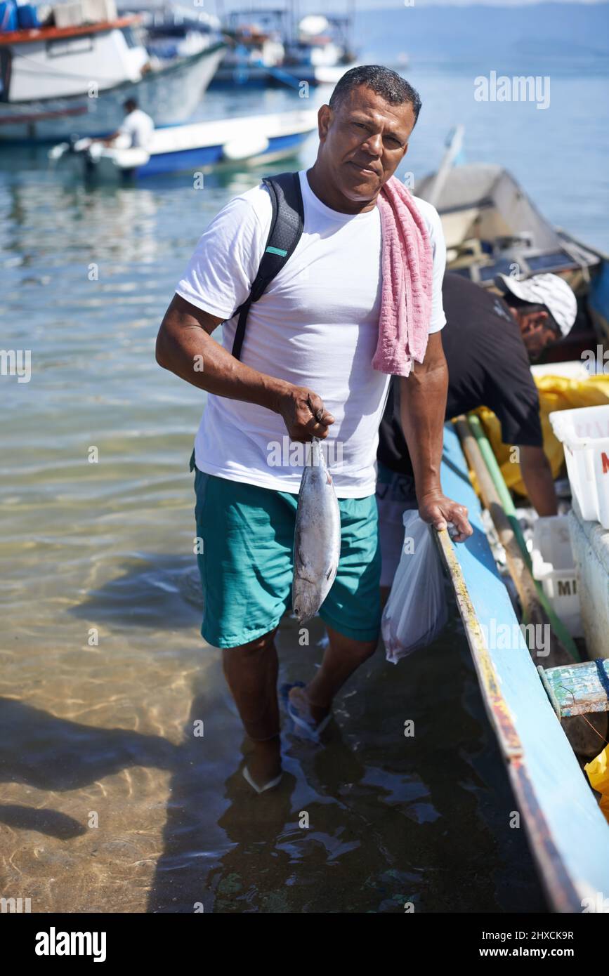 La pesca è la mia vita. Ritratto di un pescatore in piedi in acqua accanto alla sua barca. Foto Stock