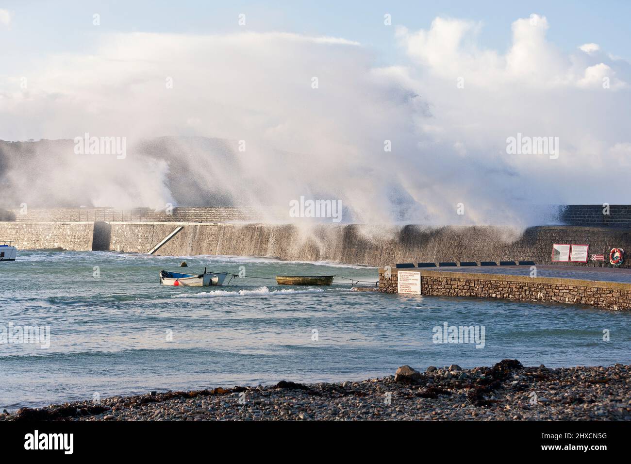 L'onda della tempesta si rompe sulle mura del porto di Goury Foto Stock