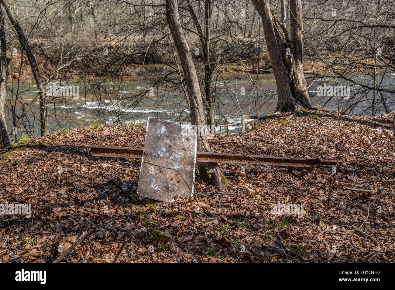 Un vecchio segno di metallo dimenticato nei boschi lungo il sentiero al fiume arrugginito e vuoto pieno di buchi giacenti sul terreno circondato da caduti Foto Stock