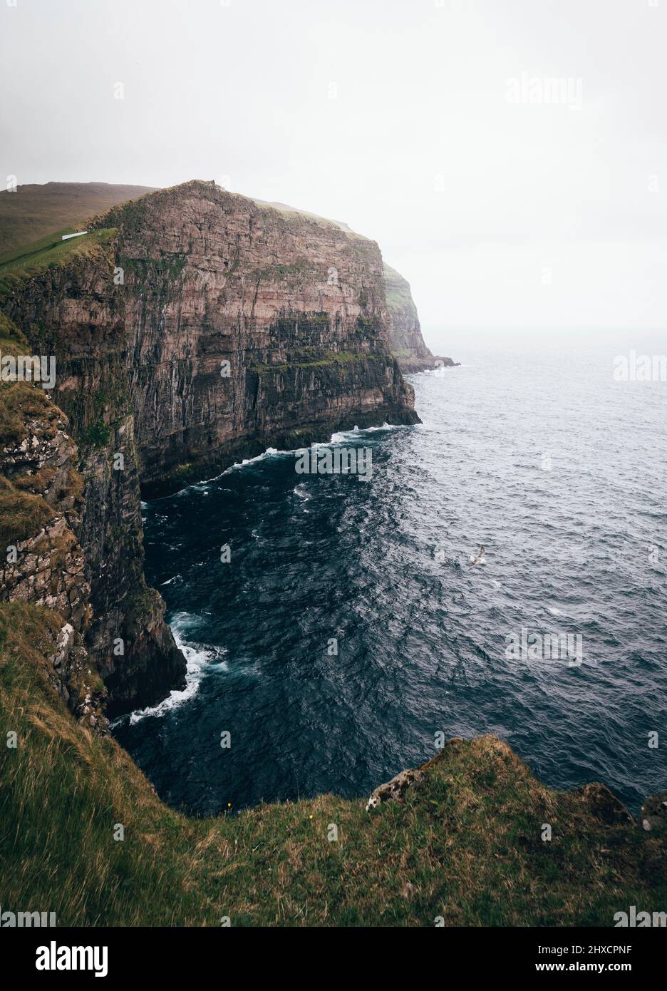 Ampie e verdi scogliere sulle Isole Faroe con onde che colpiscono la linea costiera Foto Stock