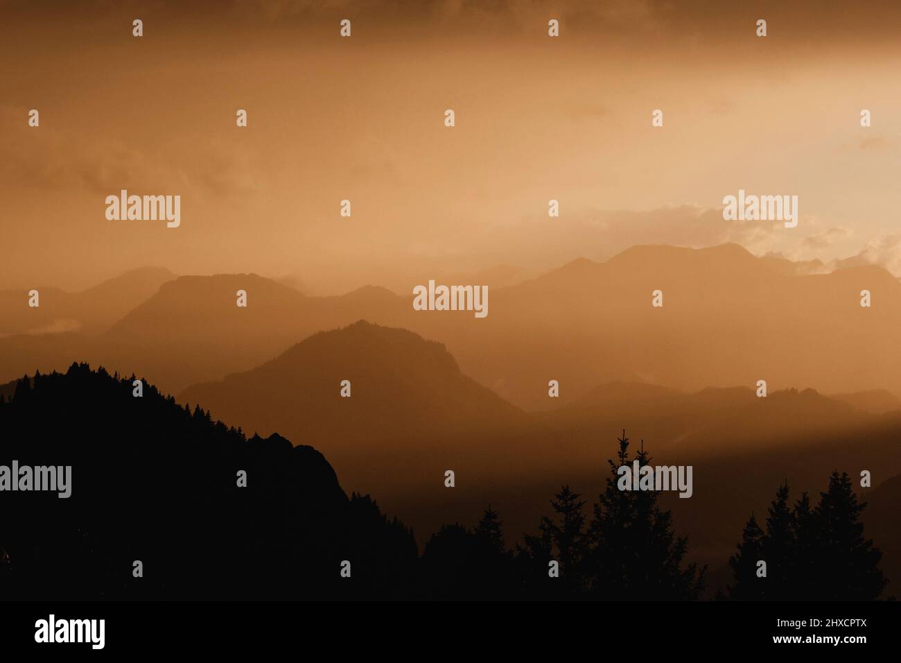 La luce del sole colpisce strati di montagne e nuvole durante l'ora d'oro Foto Stock