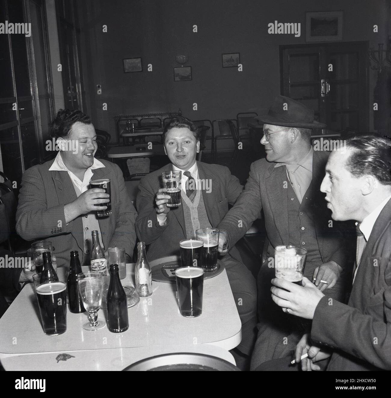 1950s, storico, cheers boyos, quattro acciaierie gallesi che hanno una buona bevanda dopo una dura giornata di lavoro, seduti intorno a un tavolo presso il club sociale del complesso d'acciaio Abbey Works, Port Talbot, Galles, Regno Unito Foto Stock