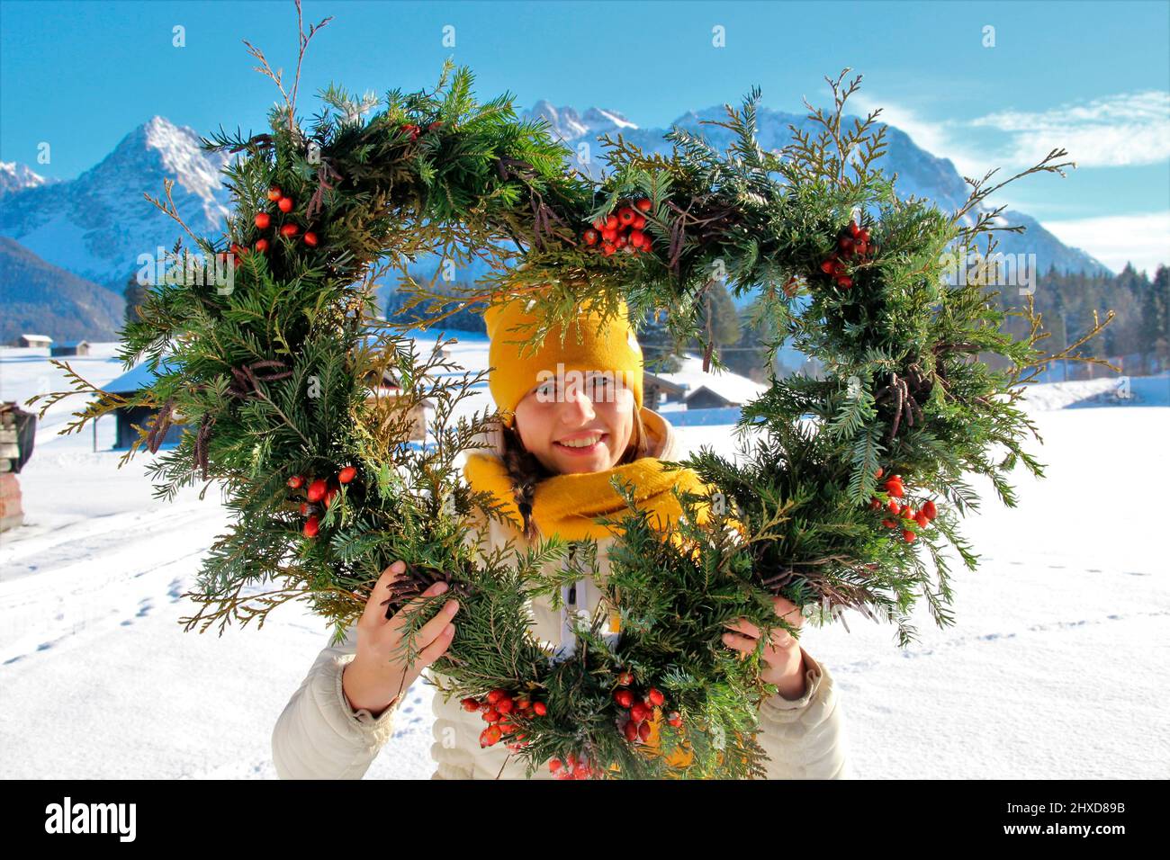 Giovane donna con cuore deco di fronte al panorama montano, Karwendel, neve d'inverno, cuore, allegro, Mittenwald, Germania, Baviera Foto Stock