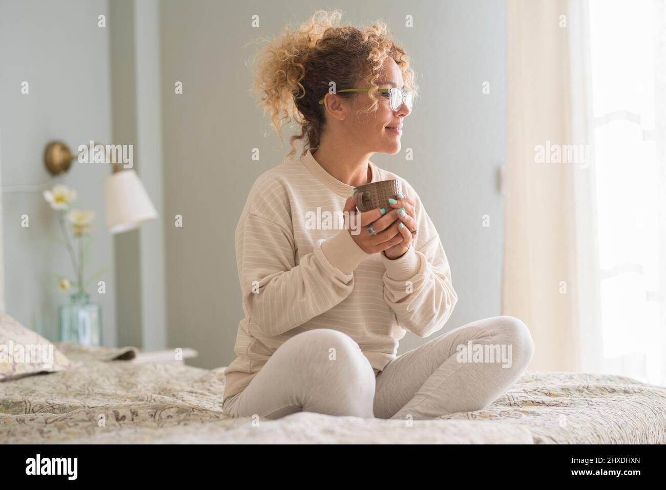 Buon risveglio positivo mattina donna adulta seduta sul letto e bere sorridente alla luce della finestra. Le donne di stile di vita sano godere di nuovo giorno comi Foto Stock