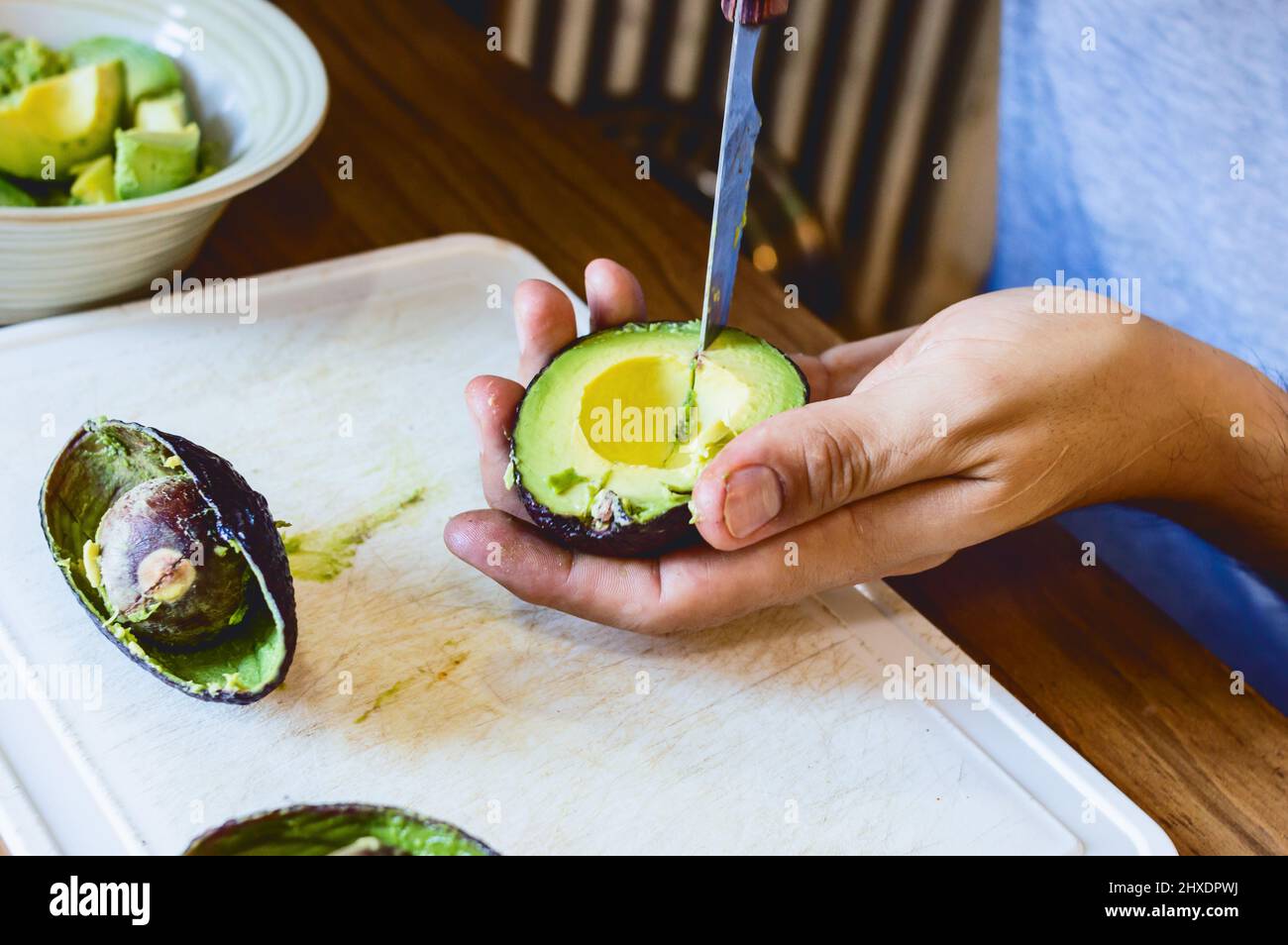 primo piano di mani caucasiche maschili pelando un avocado con un coltello su un tagliere bianco Foto Stock