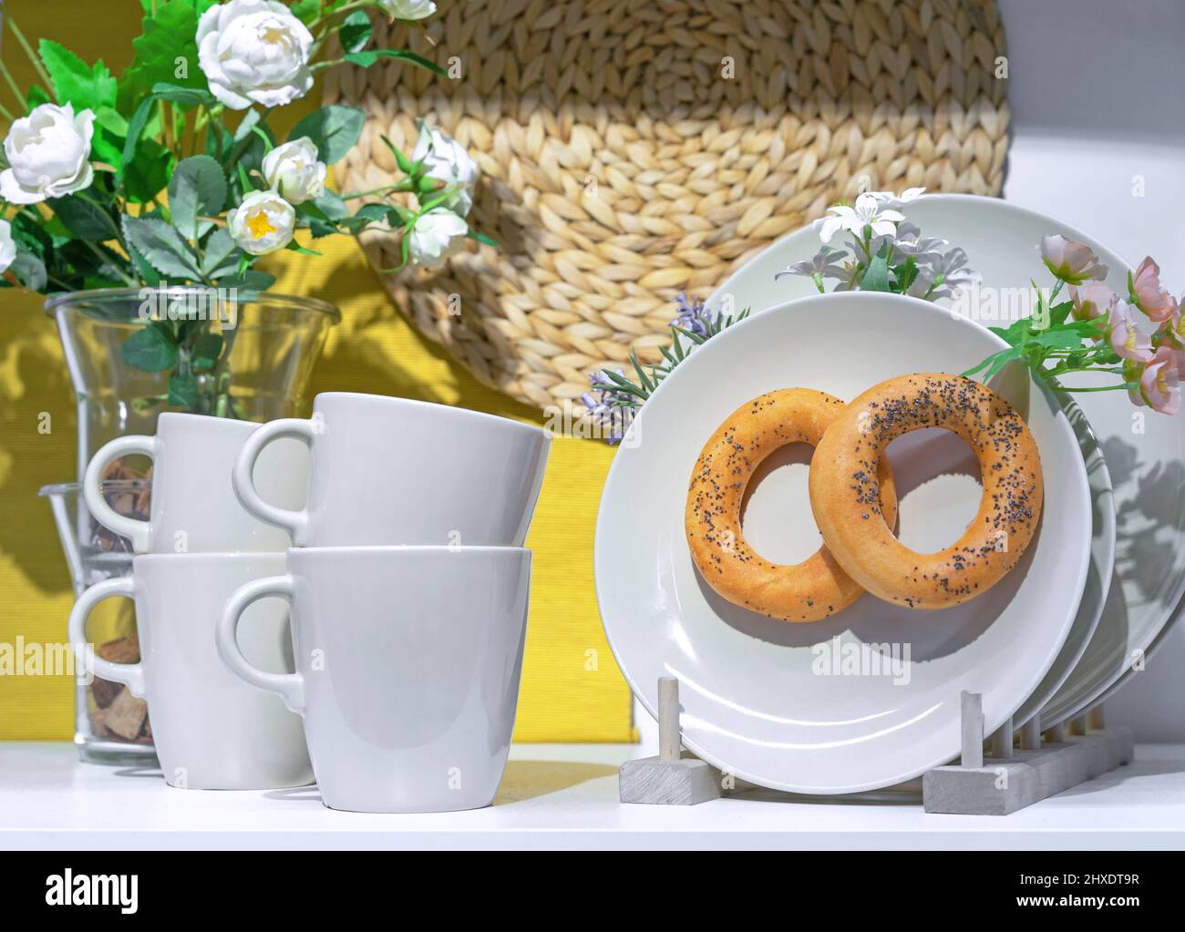 Tazze e piattino in ceramica bianca con bagel con semi di papavero. Foto Stock