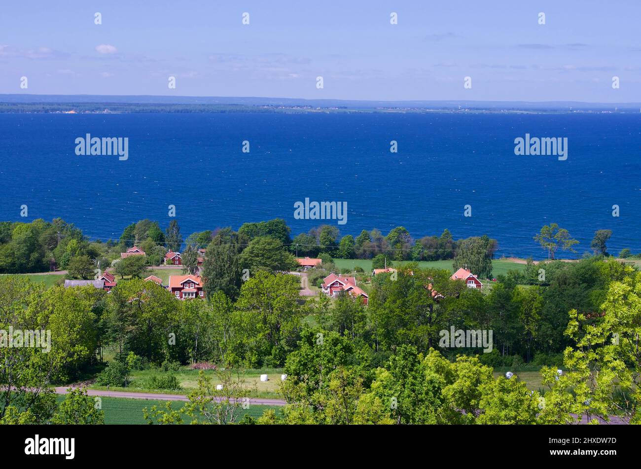 Vista su un paesaggio lussureggiante con edifici di fronte al lago Vättern e l'isola Visingsö in Svezia. Foto Stock