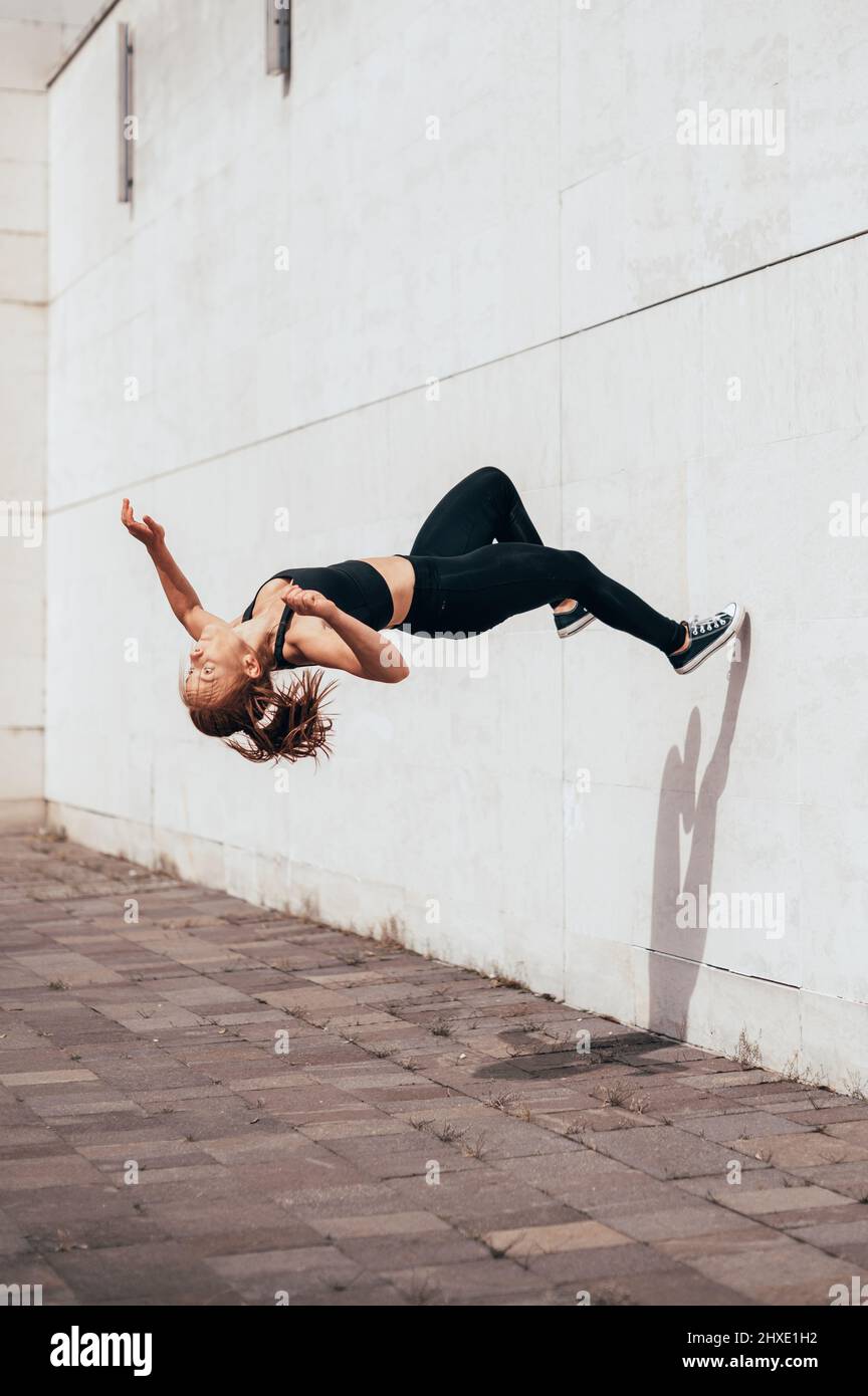 Giovani donne Parkour e Freerunning che fanno un backflip da un muro in uno sfondo urbano, saltando tumbling Ginnastica idea di formazione Foto Stock