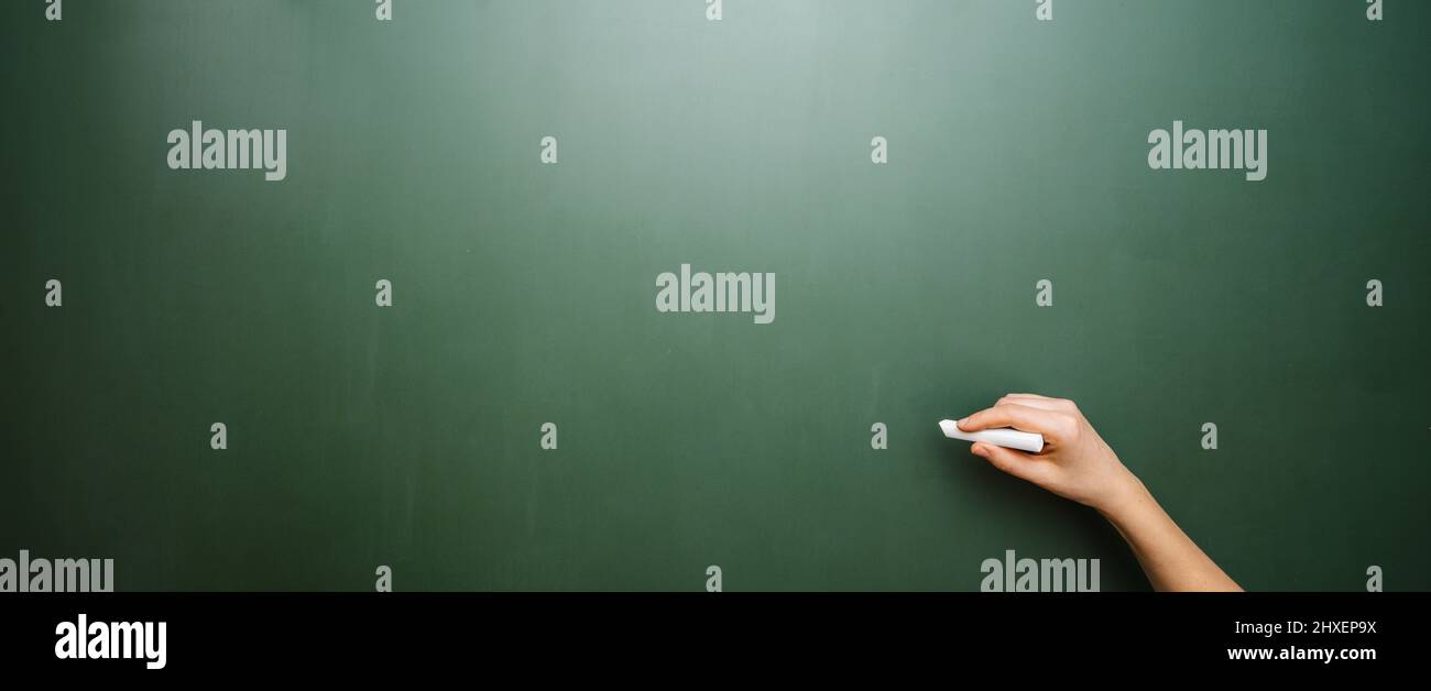 Mano di un insegnante che disegna una linea bianca con il gesso su una lavagna verde, con copyspace per il vostro testo individuale. Foto Stock