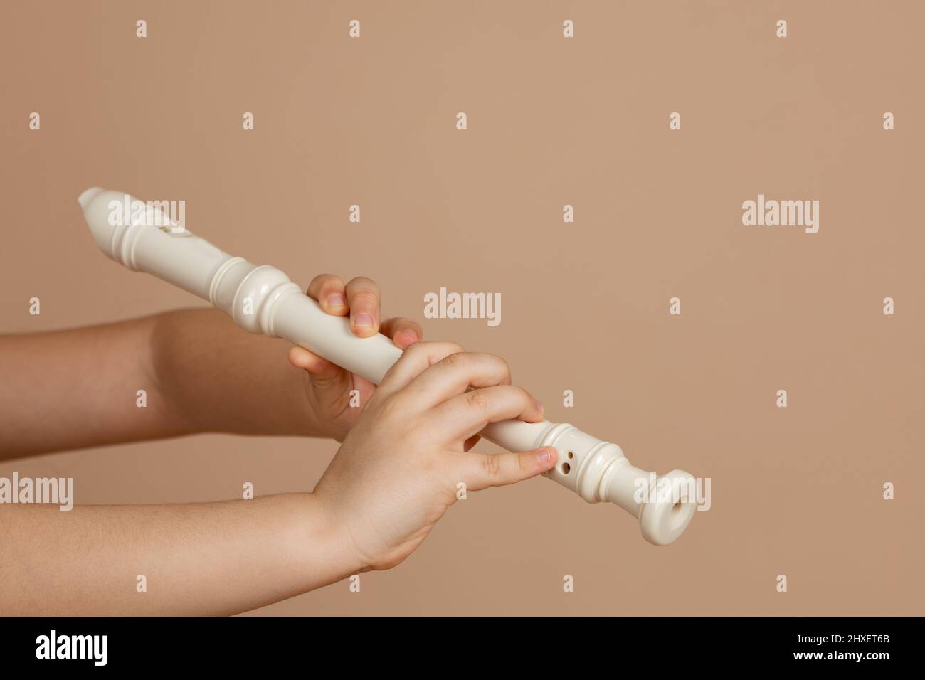 Tenere flauto fipple con entrambe le mani e buchi pizzicare primo piano, sfondo beige. Strumento musicale Woodwind. Foto Stock