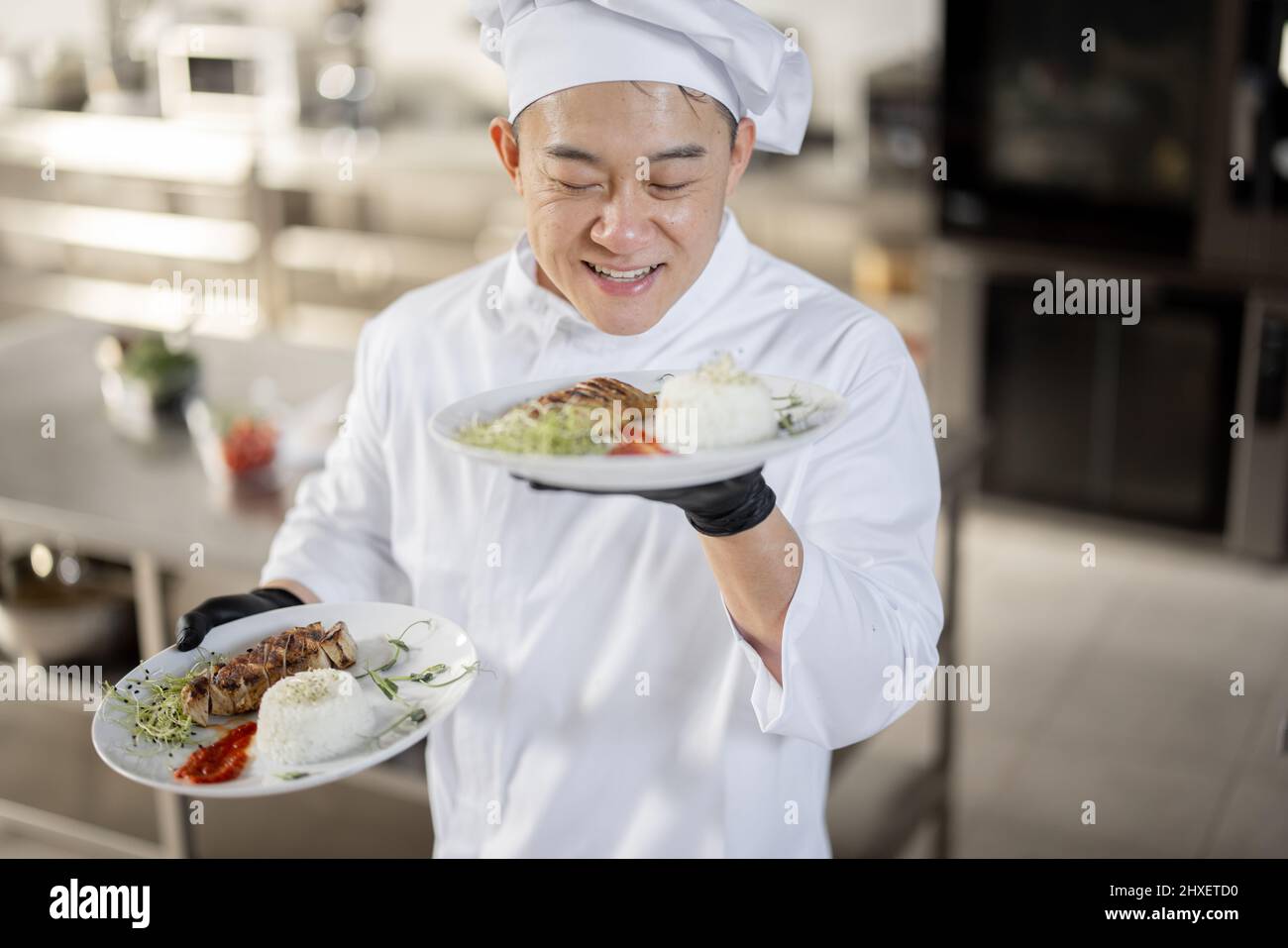 Ritratto di giovane felice bello chef sorridente in uniforme in piedi con pasto pronto in cucina. Buon cucina asiatica che lavora al ristorante. Concetto di occupazione professionale e alta cucina Foto Stock