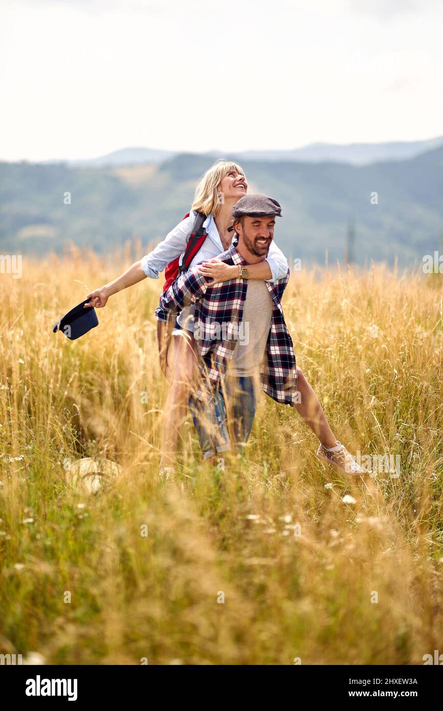 Giovane coppia di trekking caucasico gioioso in campo sorridendo e divertirsi. Ragazza piggybacking. Sport, amore, libertà, concetto di vacanza. Foto Stock