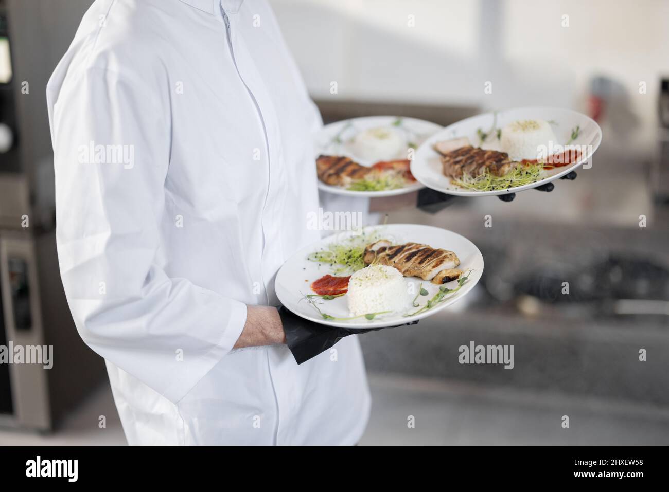 Chef che tiene tre piatti con pasti pronti, portandoli a mano. Vista ritagliata senza volto, primo piano. Concetto di servire cibo per il ristorante e l'alta cucina Foto Stock