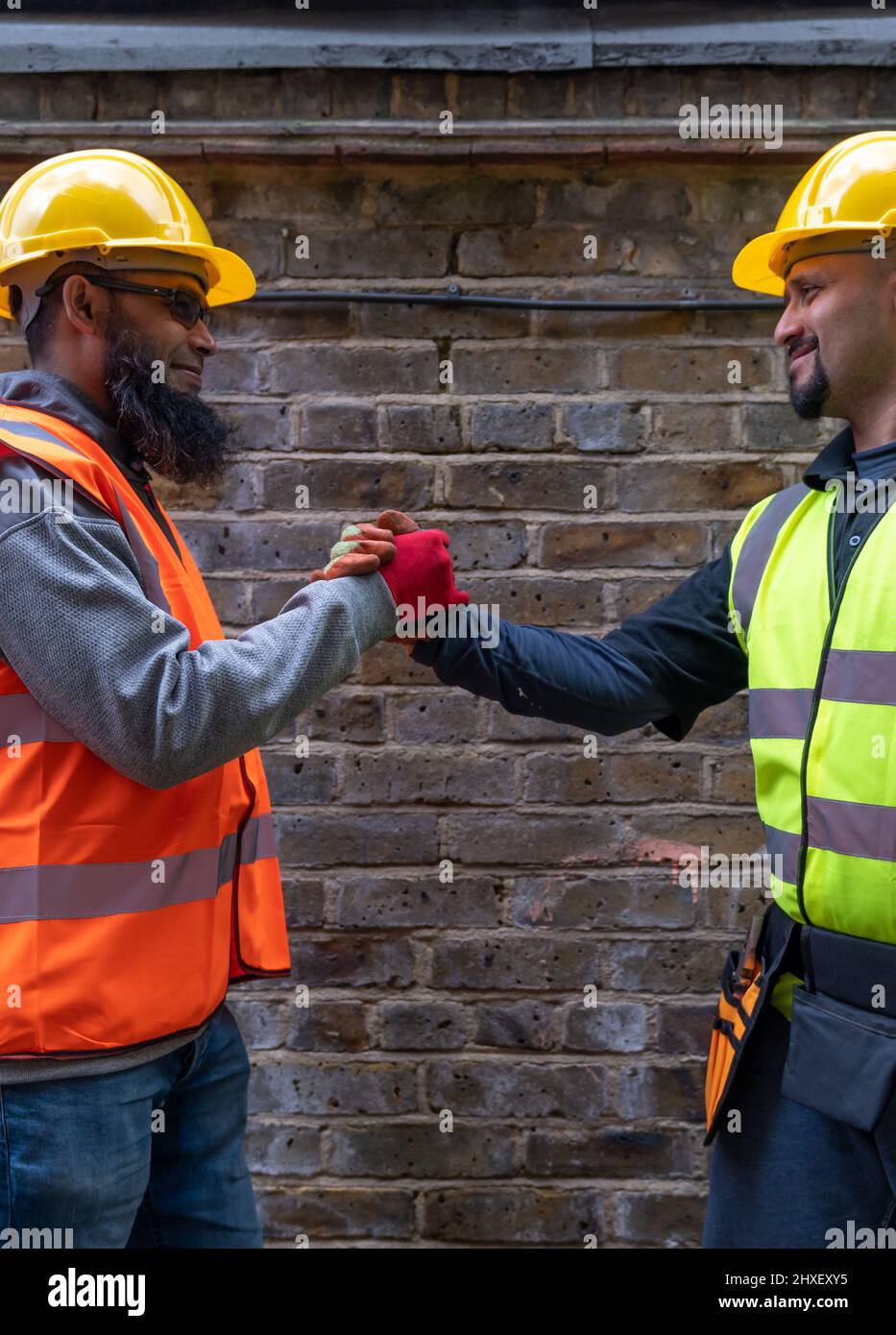 gli operai di costruzione amichevoli, felici e sorridenti salutano e scuotono le mani. Foto Stock