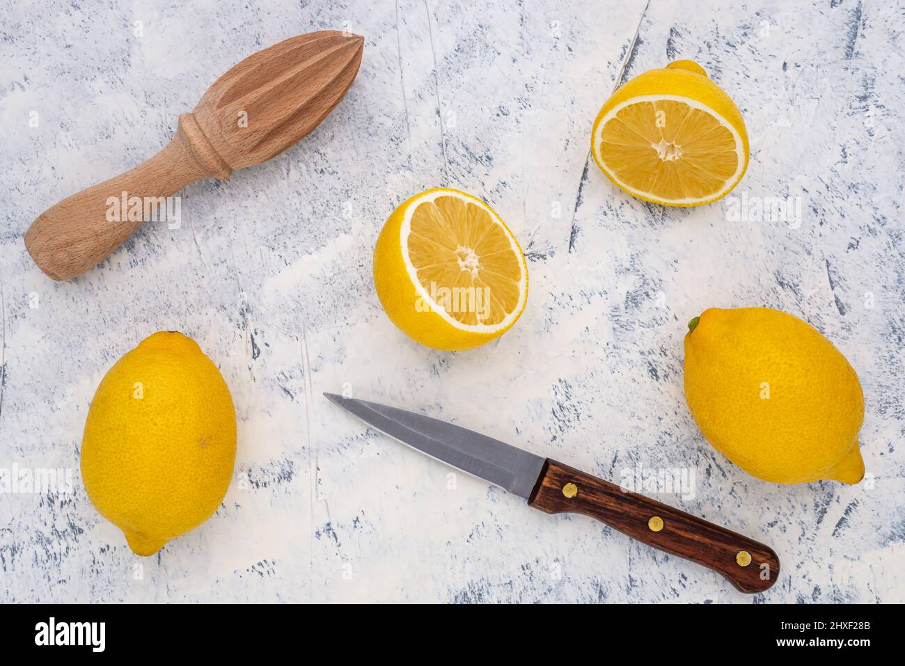 Limone fresco tagliato a metà con coltello da cucina e centrifuga su sfondo bianco-grigio. Vista dall'alto. Foto Stock