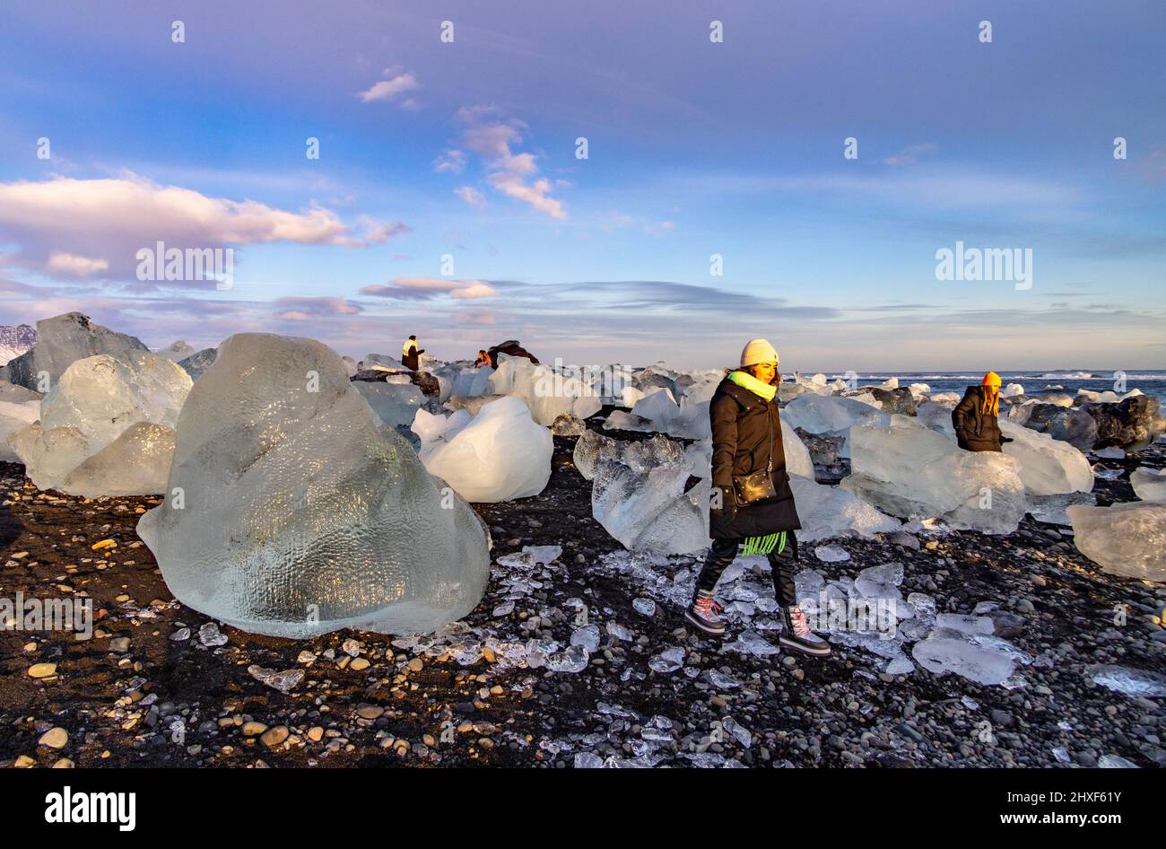 I turisti che camminano accanto agli iceberg vicino al tramonto sulla spiaggia di Diamante, Breidamerkursandur, Islanda sud-orientale Foto Stock