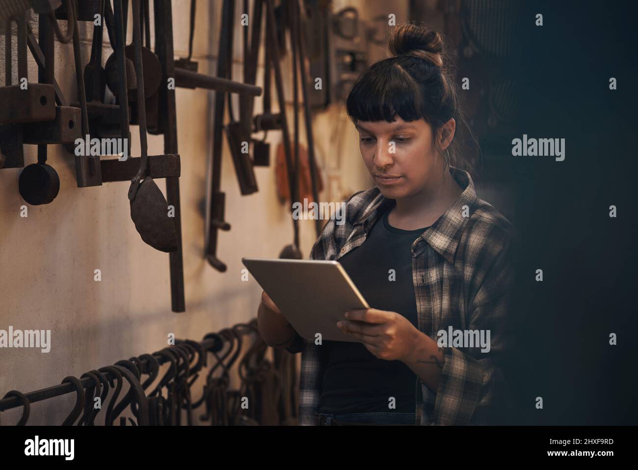 Il commercio della vecchia scuola incontra la nuova tecnologia scolastica. Scatto di una giovane donna che usa un tablet digitale mentre lavora in una fonderia. Foto Stock
