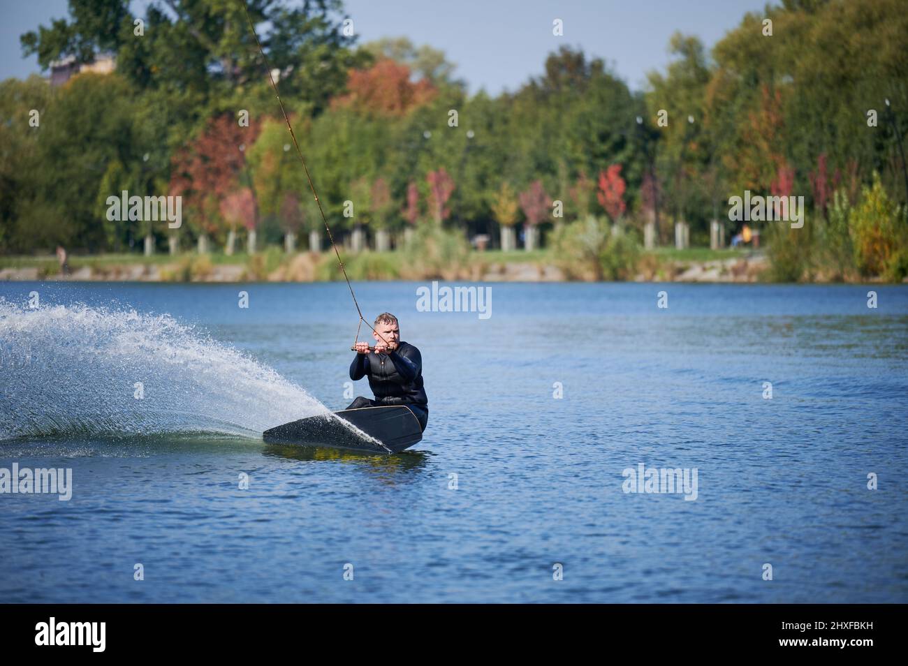 Wakeboarder surf sul lago. Giovane surfista che si diverte a prendere il wakeboarding nel parco della funivia. Sport acquatici, attività all'aperto. Foto Stock