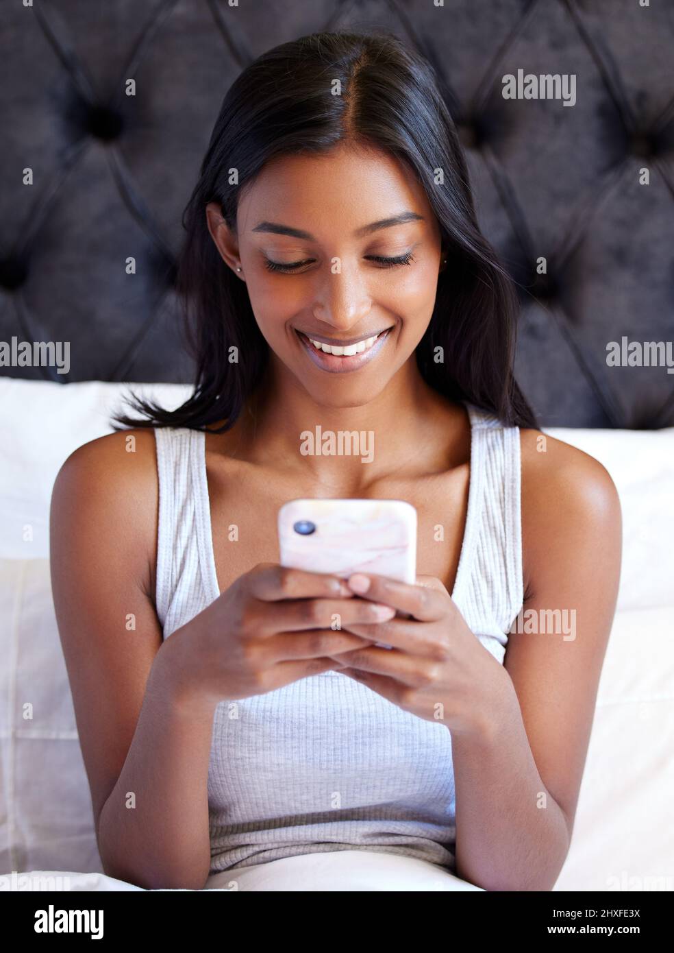 Non riesco a ottenere abbastanza di questa app. Scatto di una giovane donna usando il suo cellulare mentre si siede sul suo letto. Foto Stock
