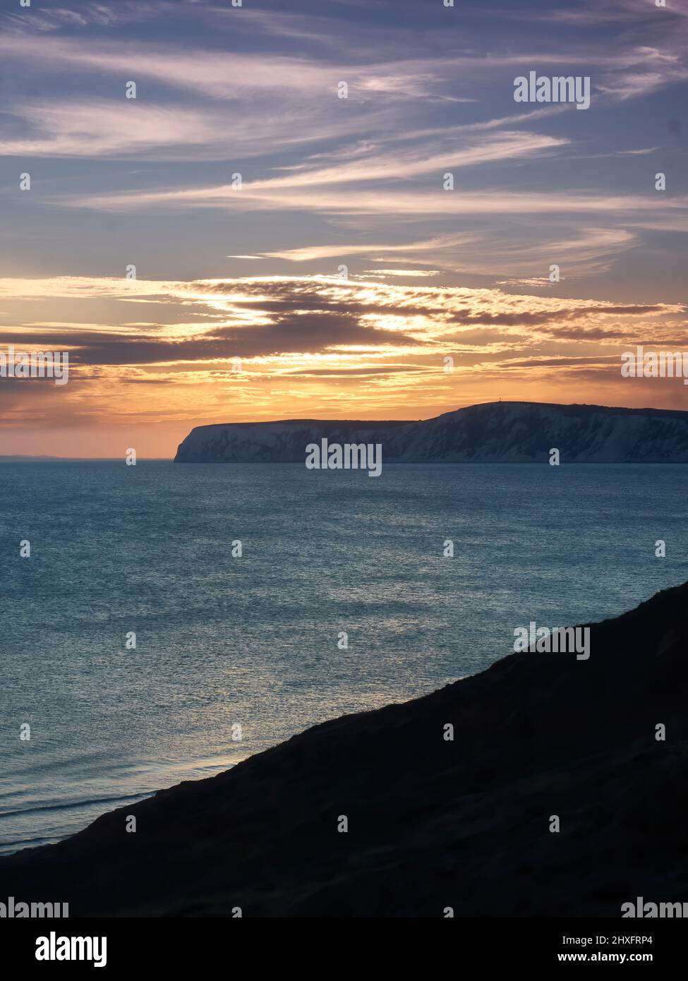 Un radioso e glorioso tramonto sul mare e sulle promontori di una scogliera di gesso dell'Isola di Wight, con i ricchi raggi dorati riflessi nelle acque testurizzate. Foto Stock