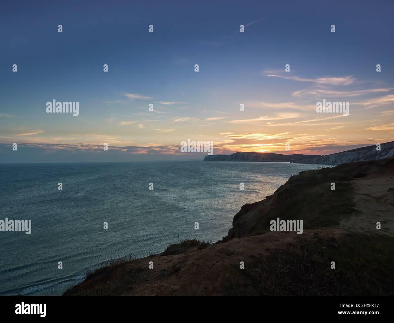 Un radioso e glorioso tramonto sul mare e sulle promontori di una scogliera di gesso dell'Isola di Wight, con i ricchi raggi dorati riflessi nelle acque testurizzate. Foto Stock