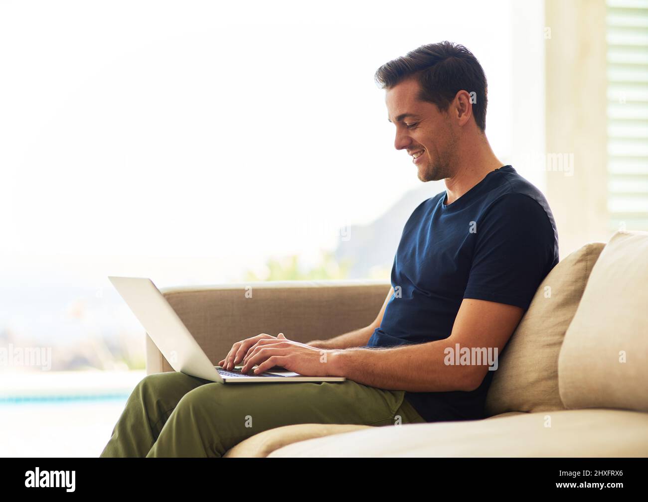 Spendendo alcuno del suo tempo libero guadagnato bene in linea. Scatto di un bel giovane uomo usando il suo computer portatile mentre si siede sul divano a casa. Foto Stock