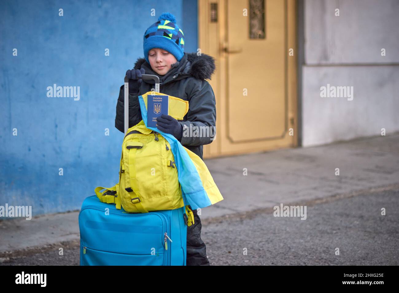 Evacuazione di civili, triste bambino con la bandiera dell'Ucraina. Famiglia di rifugiati ucraini che attraversa il confine. Mano che tiene un passaporto sopra il luggag Foto Stock