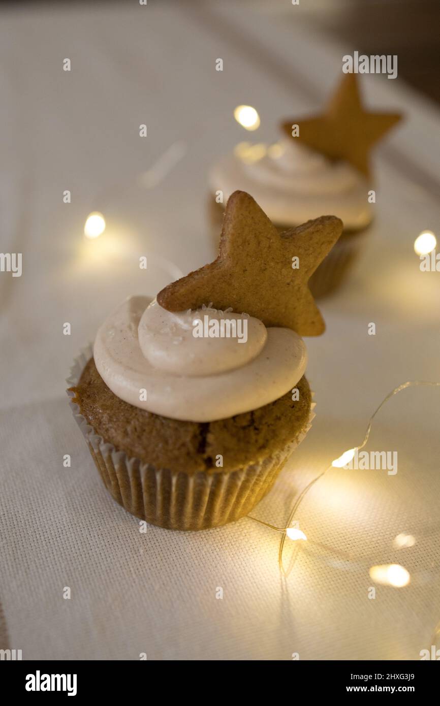 Due cupcake con decorazione dei biscotti stellari, luci scintillanti, tovaglia bianca Foto Stock