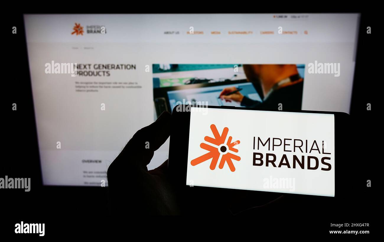 Persona che tiene il cellulare con il logo della società britannica di tabacco Imperial Brands plc sullo schermo di fronte al sito web aziendale. Mettere a fuoco sul display del telefono. Foto Stock