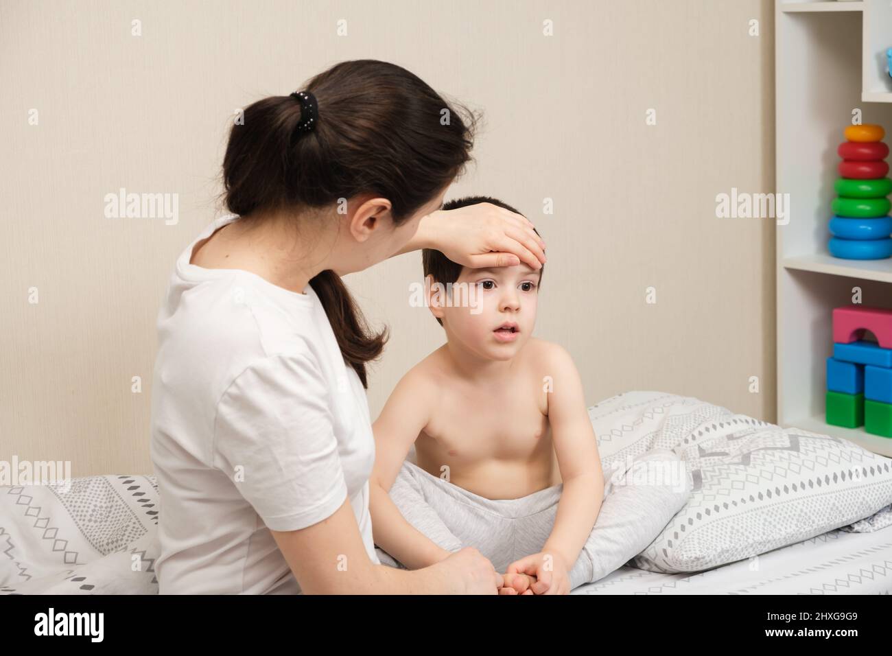 La madre misura la temperatura di un bambino malato, mette la mano sulla fronte. Malattie con febbre nei bambini, influenza o coronavirus Foto Stock